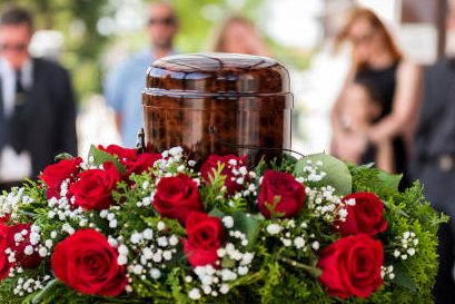 Eine mit Rosen und Weißdorn geschmückte Urne auf einem Urnenpult.