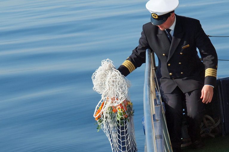 Ein Kapitän läst eine Urne und Blumen zu Wasser.